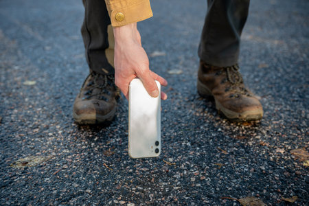 Close-up of man in boots picking up his broken smartphone with cracked screen glassの写真素材