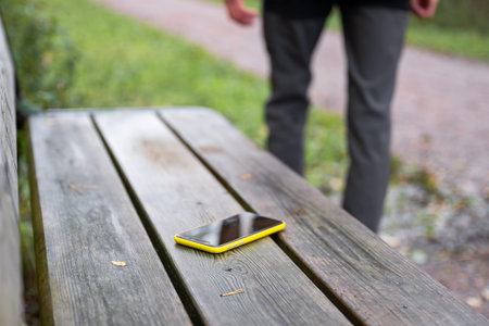 man is leaving from a bench where he lost his smartphone. Forgotten smartphone on a park bench.