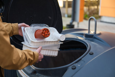 man throwing out plastic garbage into recycling bin outsideの写真素材