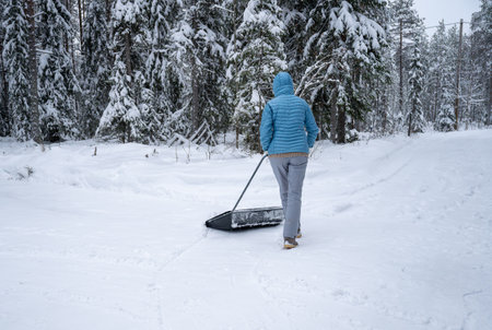 Woman in winter clothing clearing snow with scraper outdoorsの写真素材