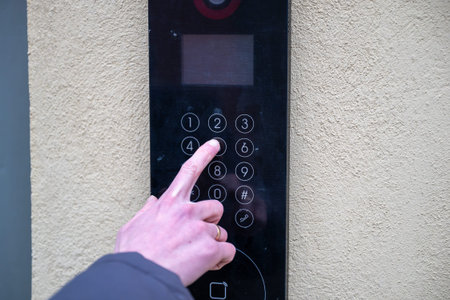 Close-up of a hand pressing a button on a digital intercom keypad, concept of security and access...