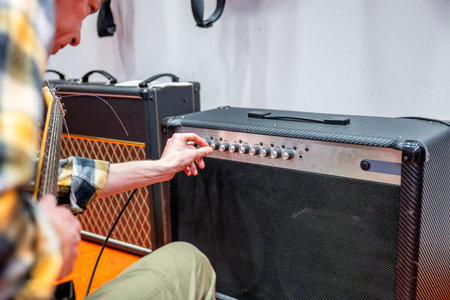 Guitarist adjusting settings on amplifier of electric guitar in recording studio