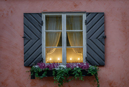Elegant window with black shutters, glowing candles, floral decor, and pink background