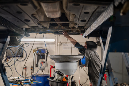 Mechanic inspecting a car on a hydraulic lift in a garage, with tools and equipment in the background. Concept of vehicle maintenanceの写真素材