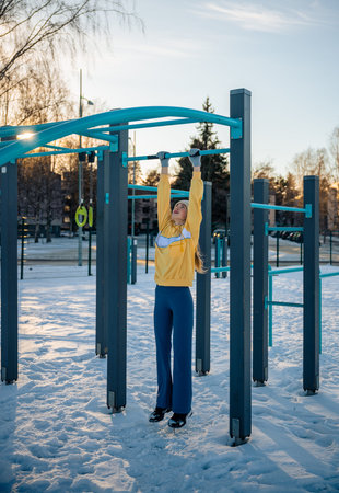 Young woman exercising on monkey bars in winter outdoor gym