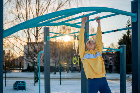 Young woman exercising on monkey bars in winter outdoor gym