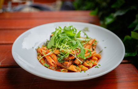 Penne pasta with tomato sauce and arugula served on white plate outdoorsの写真素材