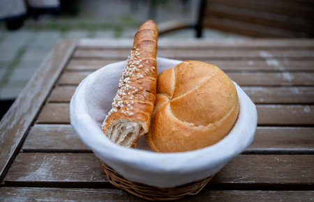 Two types of fresh bread rolls in wicker basket on wooden outdoor table surfaceの写真素材