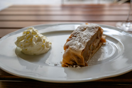 Apple strudel slice with whipped cream on white plate on wooden table surfaceの写真素材