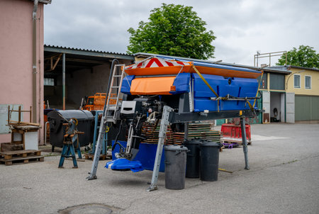 Industrial road salt spreader stored on support legs in maintenance yard outdoors
