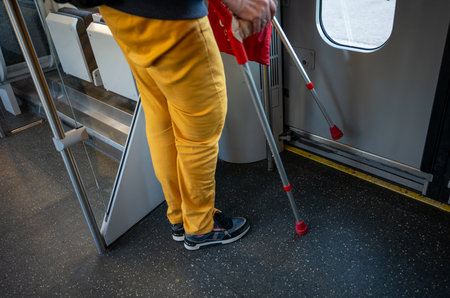 Person with crutches standing inside public transportation, showing accessibility and mobility aidの写真素材