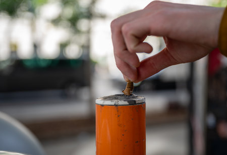 hand pressing cigarette butt against an orange public ashtray pole, concept of anti-litteringの写真素材