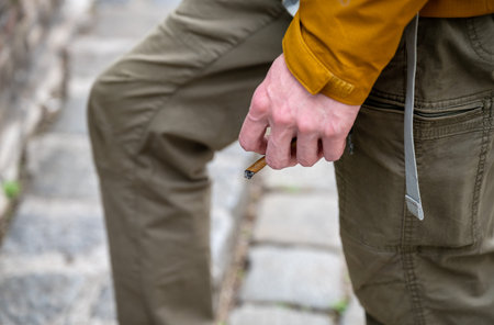 Close-up of Hand holding a burning cigarette outdoors in casual clothing