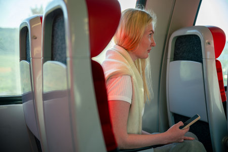 Woman using smartphone while traveling on modern train with red seatsの写真素材