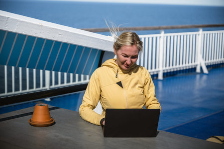 Woman working on laptop outdoors on ferry deck on sunny windy day