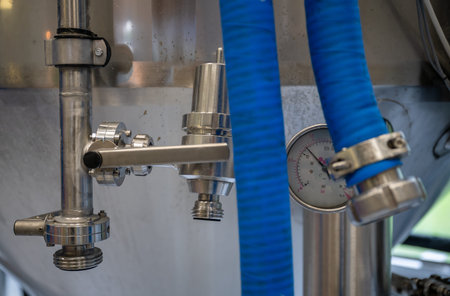 Stainless steel tap and pressure gauge at modern craft brewery with blue hose