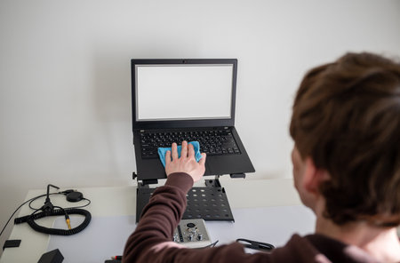 Person cleaning laptop screen with microfiber cloth on adjustable desk stand in home office