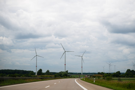 Wind turbines along highway under cloudy sky on summer day, renewable energy landscape