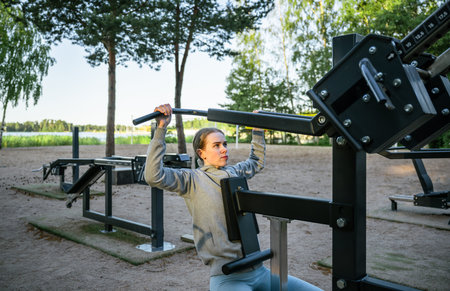 Young woman training on outdoor gym machine in park on a sunny day
