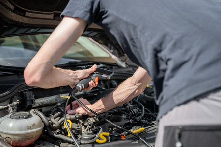 Mechanic using diagnostic tool to inspect car engine during vehicle maintenanceの写真素材