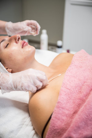 Beautician applying cosmetic treatment on female face with cotton swab in beauty salon