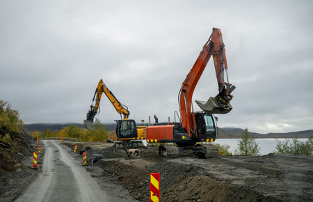 Two excavators working on rural road construction near lake in autumn landscape
