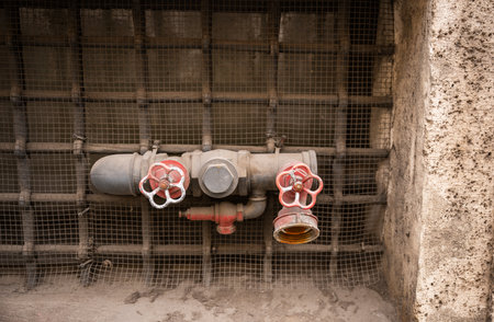 Old industrial water pipe with red valve handles against metal grid backgroundの写真素材