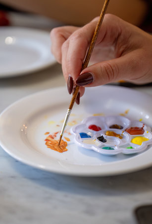 Hand mixing paint with brush on white plate and colorful paletteの写真素材
