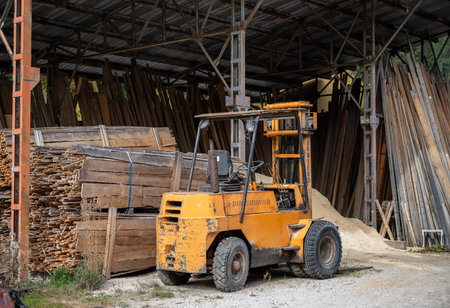 Old yellow forklift inside carpentry workshop with wooden planks and construction materialsの写真素材