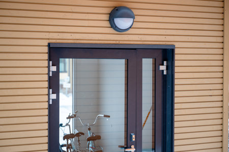 Modern glass entrance door with wall lamp on residential building exterior in winter season