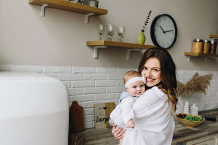 Young happy caucasian mother holding her cute baby daughter in the kitchen smilingの写真素材