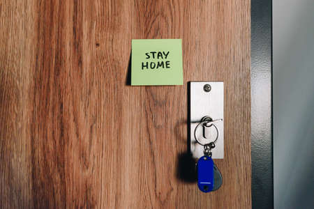 Stay at home handwritten sticky note on front door next to lock and set of keys, precaution to stay isolated during global coronavirus covid-19 pandemic and quarantineの写真素材