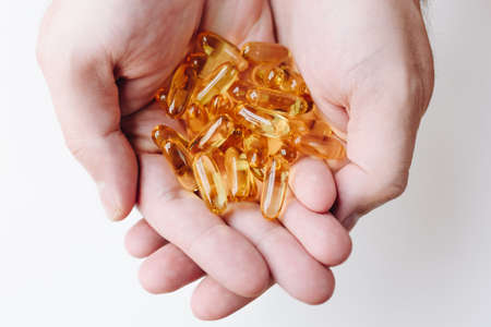 Close up of hands holding gelcap or softgel transparent capsule pills with omega 3 and vitamins c and d as medicine for immunityの写真素材