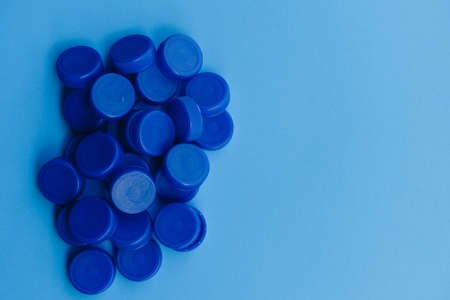 Pile of blue plastic caps from bottles isolated on blue background, concept of ocean plastic waste and pollution problem, part of the global warming and climate change crisisの写真素材