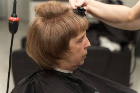 an elderly woman with brown curly hair in a beauty salon does stylingの写真素材