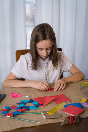 a teenage girl makes origami out of colored paper at home in the living roomの写真素材