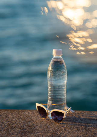beautiful summer background with a bottle of drinking water and sunglasses and the sea in the background. high quality photoの写真素材