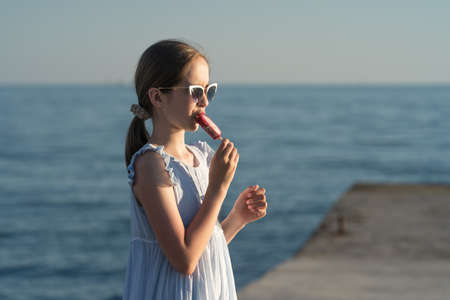 a beautiful Caucasian girl in a summer dress and sunglasses eats ice cream. High quality photoの写真素材