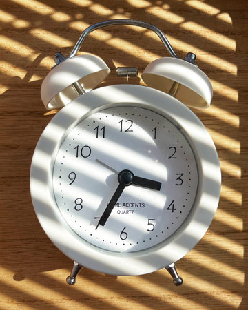 A white retro clock lies on a wooden surface with natural sun rays on it.