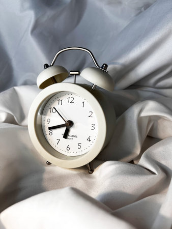 White vintage alarm clock on white textile background