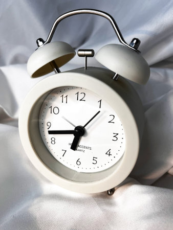 White vintage alarm clock on white textile backgroundの写真素材
