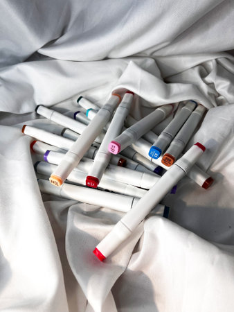 White markers of different colors are scattered across the table on white textile backgroundの写真素材