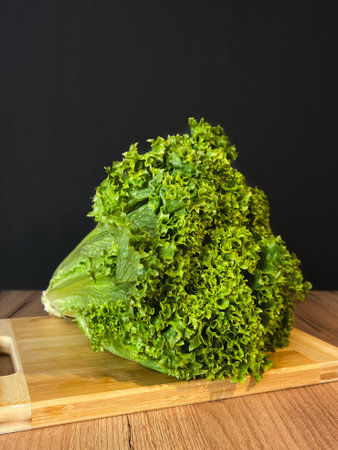 Leaf lettuce or better known as selada keriting is a type of lettuce whose leaf tips are wavy and light green in color. On a wooden board and black backgroundの写真素材