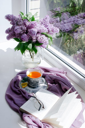 Lilac bouquet, an open book and a cup of tea on a window sill.の写真素材
