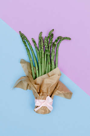 Creative spring concept as a top view shot of asparagus bouquet with kraft paper on a purple and blue background.の写真素材