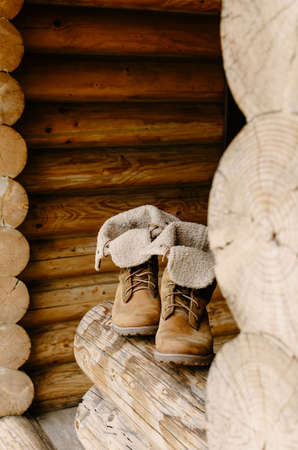 Brown hiking boots standing on a porch of a wooden country house.の写真素材