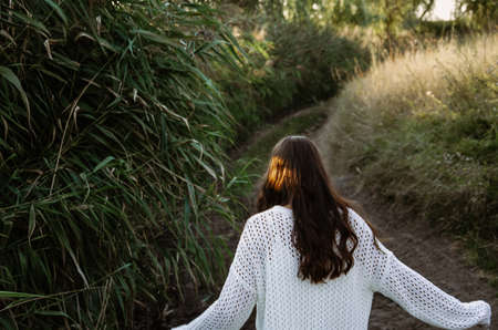 Brunette woman in a white sweater is running down the road of reeds field during sunset.の写真素材