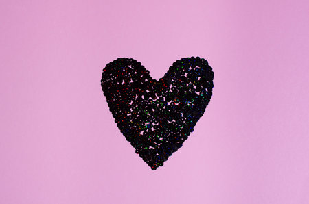 Black sequin heart shape on a pastel pink background. St. Valentines Day greeting card concept.