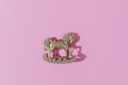 Golden and silver sparkling carousel horse Christmas decoration on a pink background with hard shadowsの写真素材