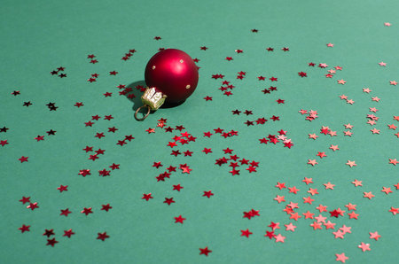 Red Christmas decoration toy ball with red star sequins sparkles on a mint green background.の写真素材
